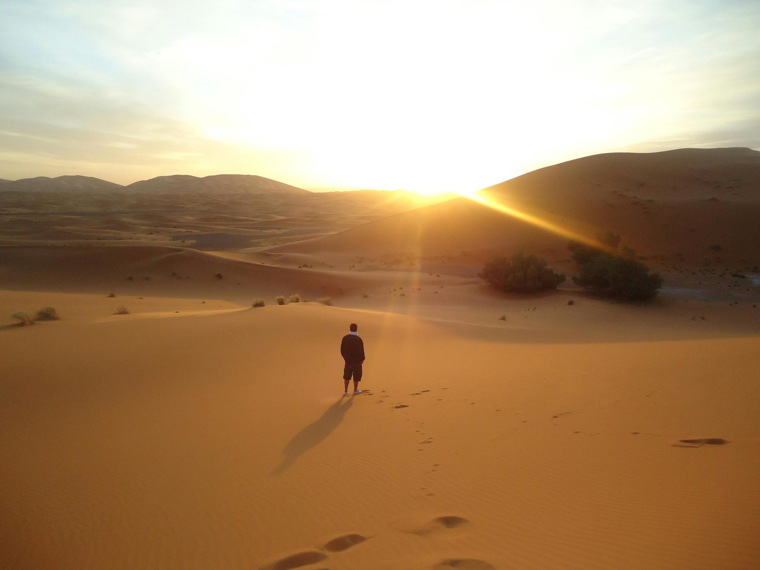 Silhouette of a man walking along sand dunes during a sunrise in the Sahara Desert.
