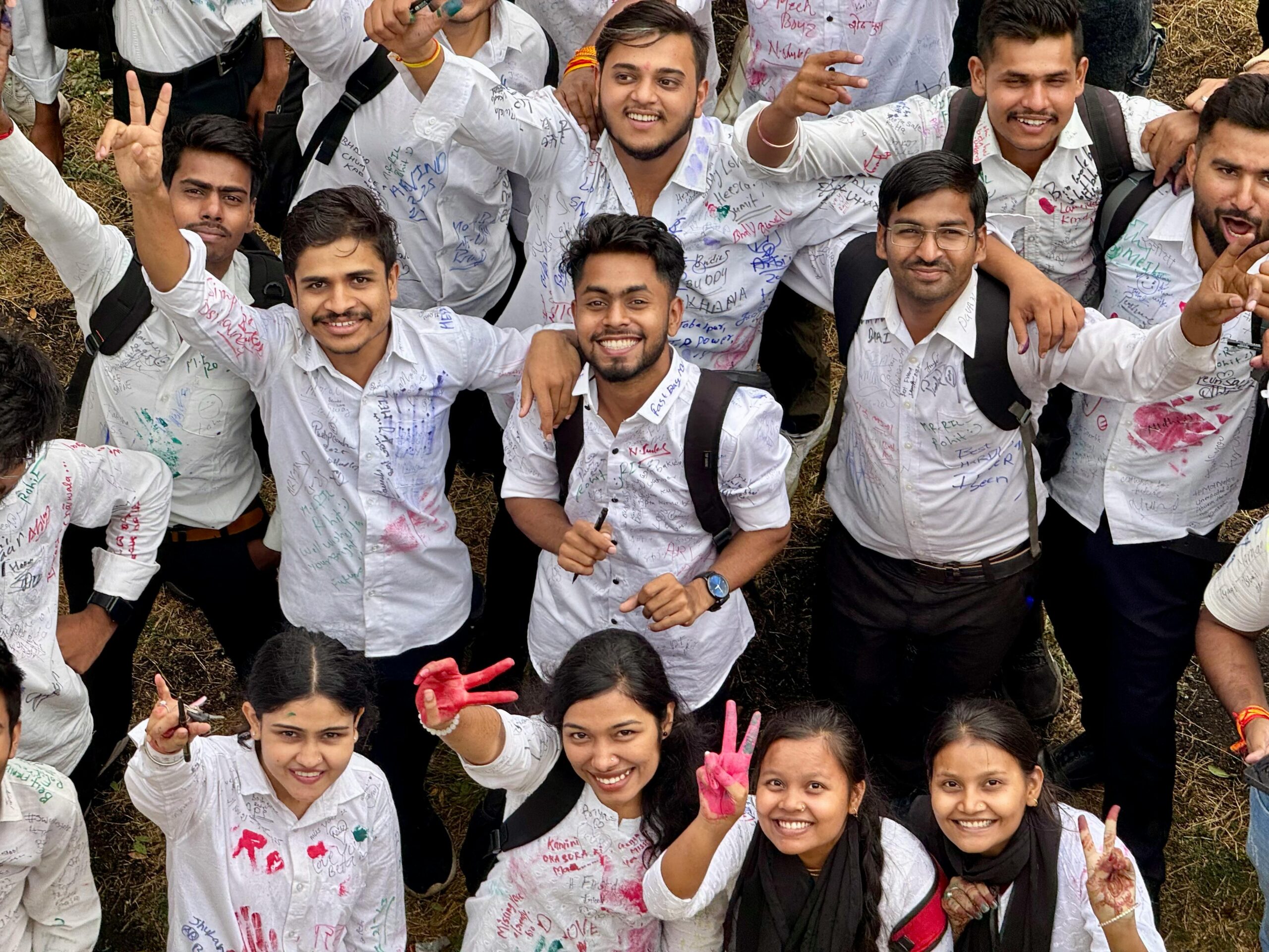 A vibrant group of college students celebrating outdoors with cheerful expressions and white shirts signed with colorful inks.