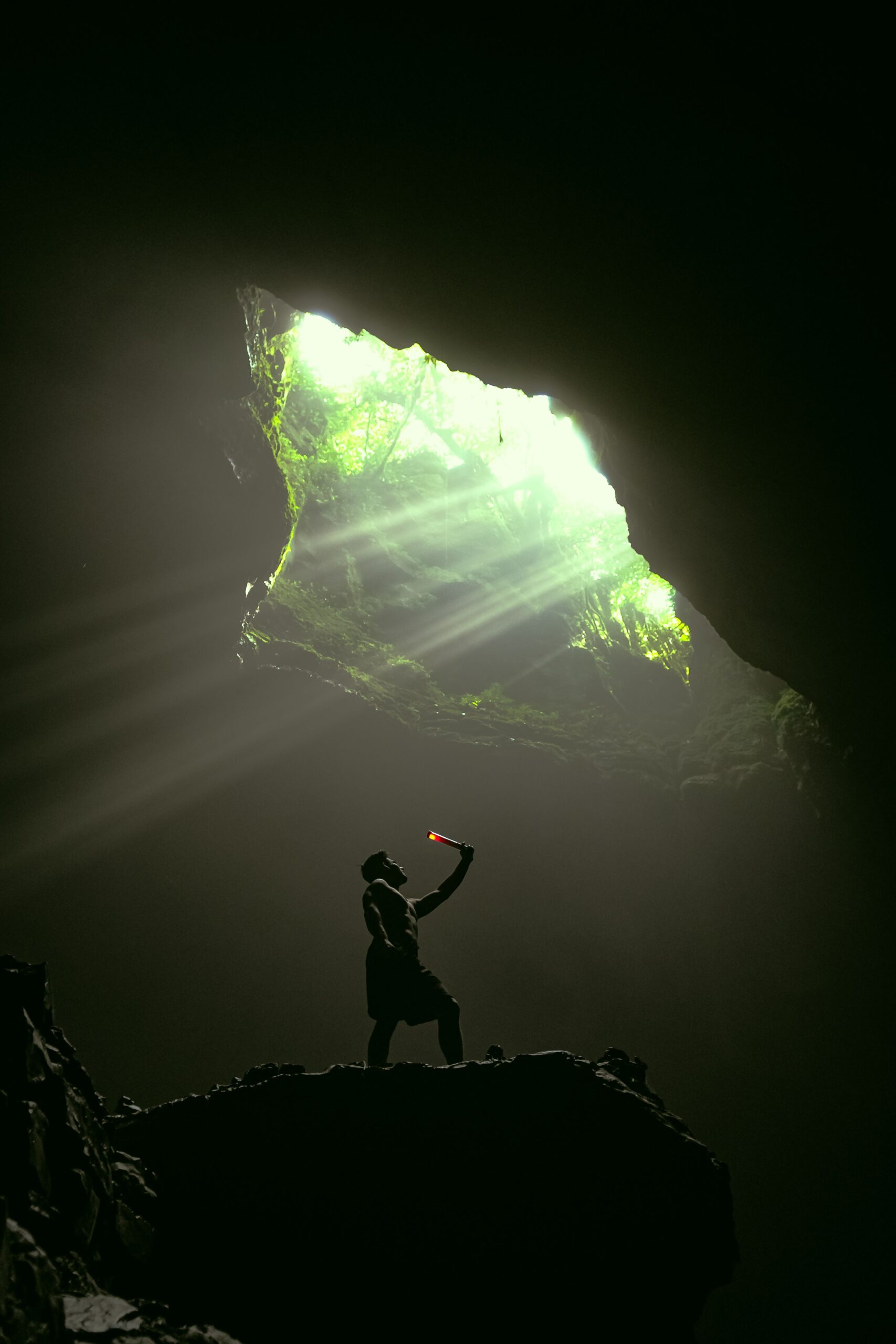 A man stands in a cave with dramatic sunlight beaming through the opening above.